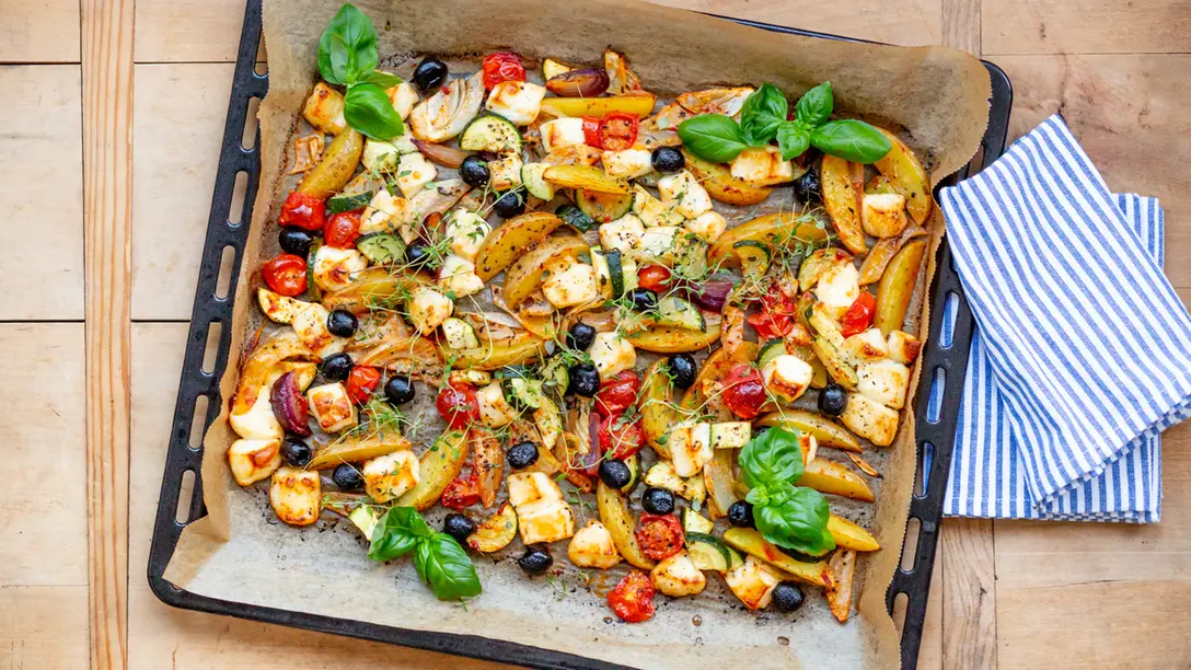 Mediterranes Ofengemüse mit Kartoffeln, Fenchel, Zucchini, Tomaten, Oliven und Halloumi auf einem Backblech